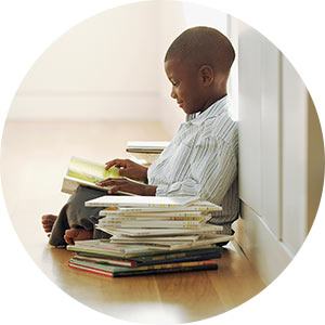 young boy sitting on floor reading books