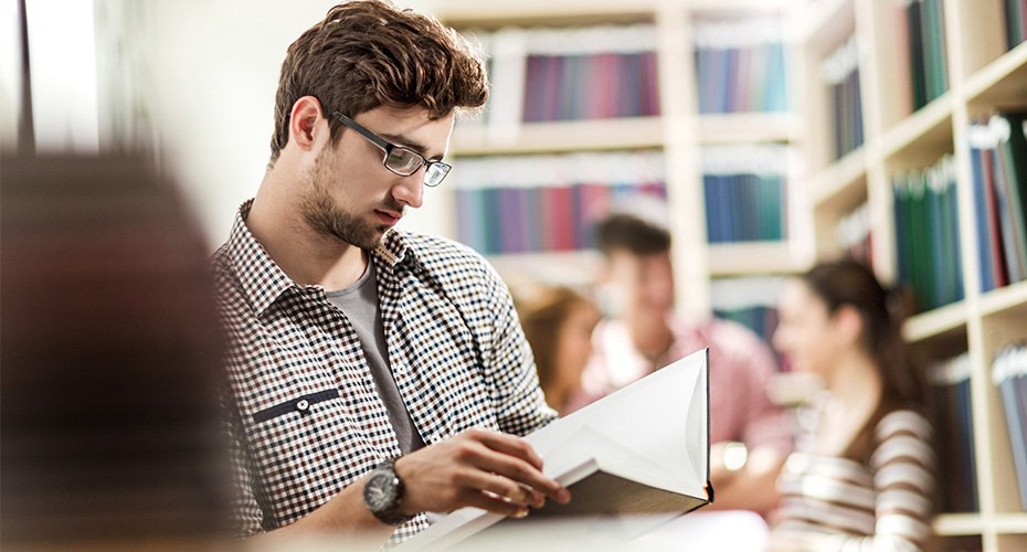 student teacher in library reading up on teacher requirements for his state