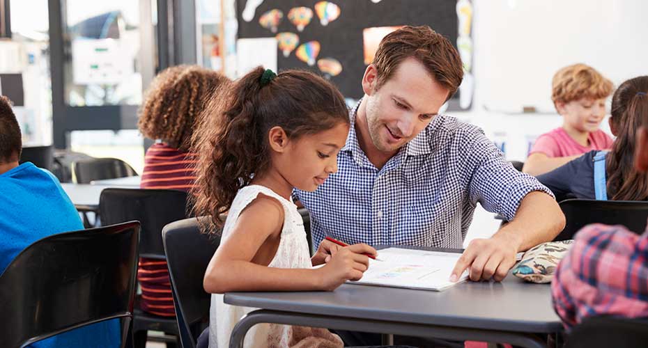 male elementary school teacher assists student with reading assignment