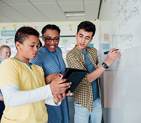 teacher instructing two high school students at whiteboard