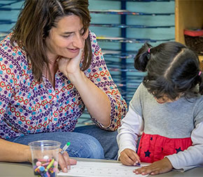 elementary teacher sitting with student coloring a picture