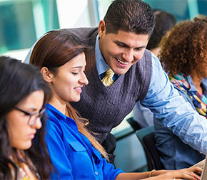teacher helping college student working on laptop computer in classroom