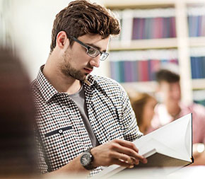 student teacher in library reading up on teacher requirements for his state