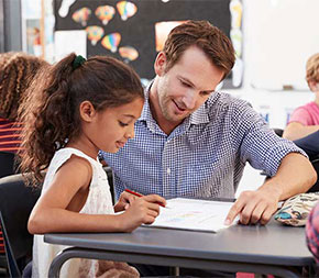 male elementary school teacher assists student with reading assignment